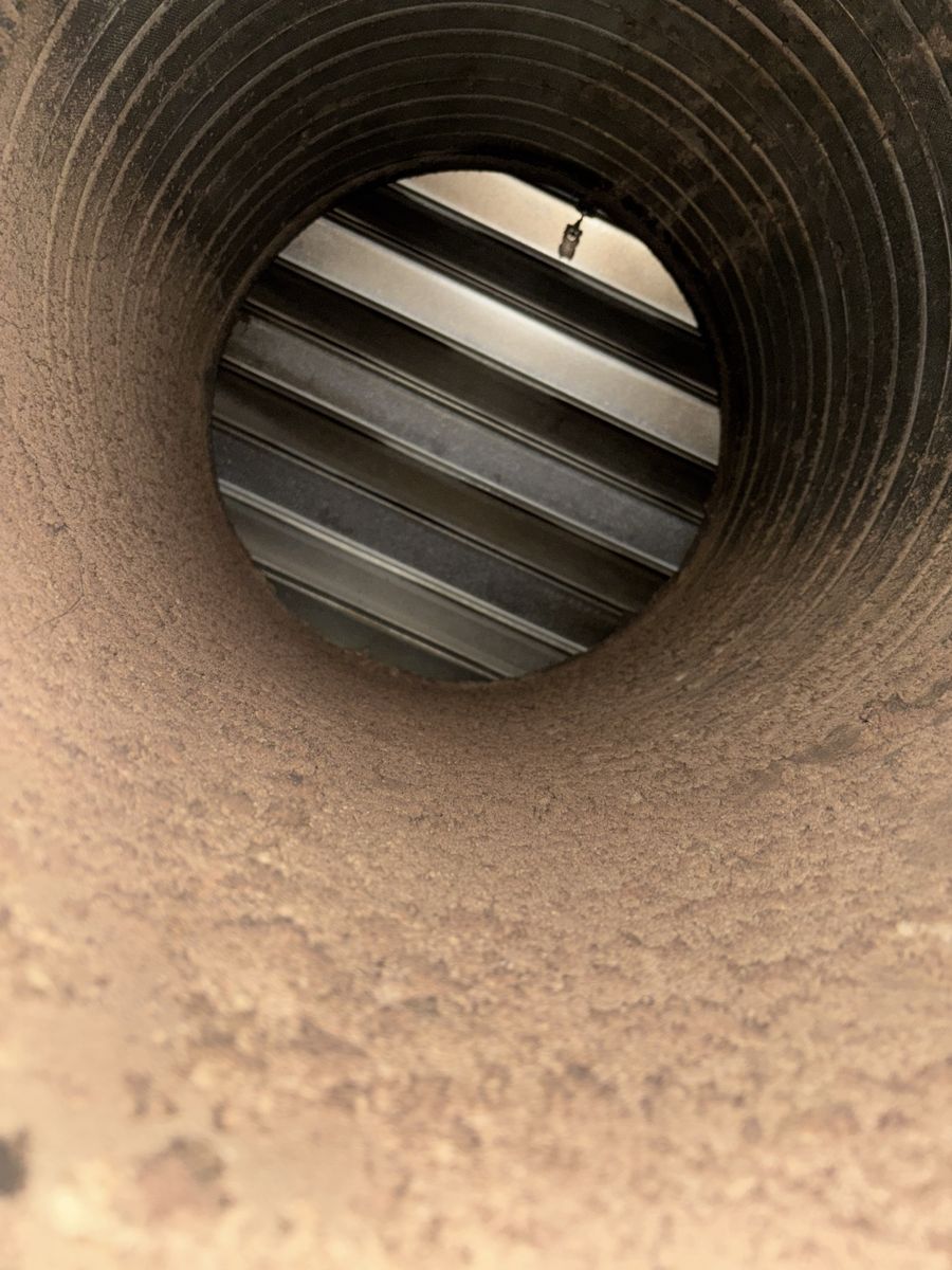 Inside a spiral furnace duct before cleaning, fine dust caked along the bottom
