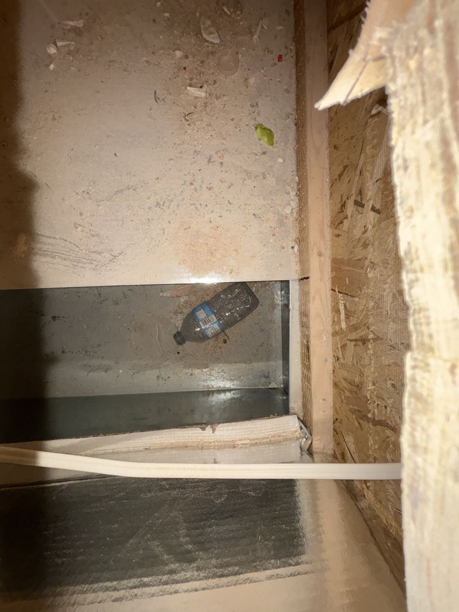 Inside a duct before cleaning, with sawdust, debris and a plastic water bottle