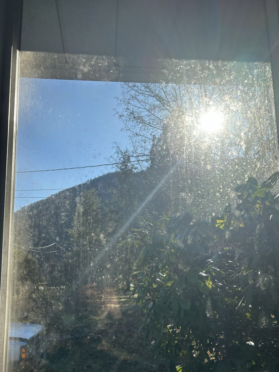 Window covered in spots and haze, lit up by the sun, before cleaning
